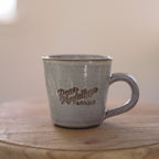 Gray ceramic mug with 'Dean Madalyn Florals' branding on a wooden surface.