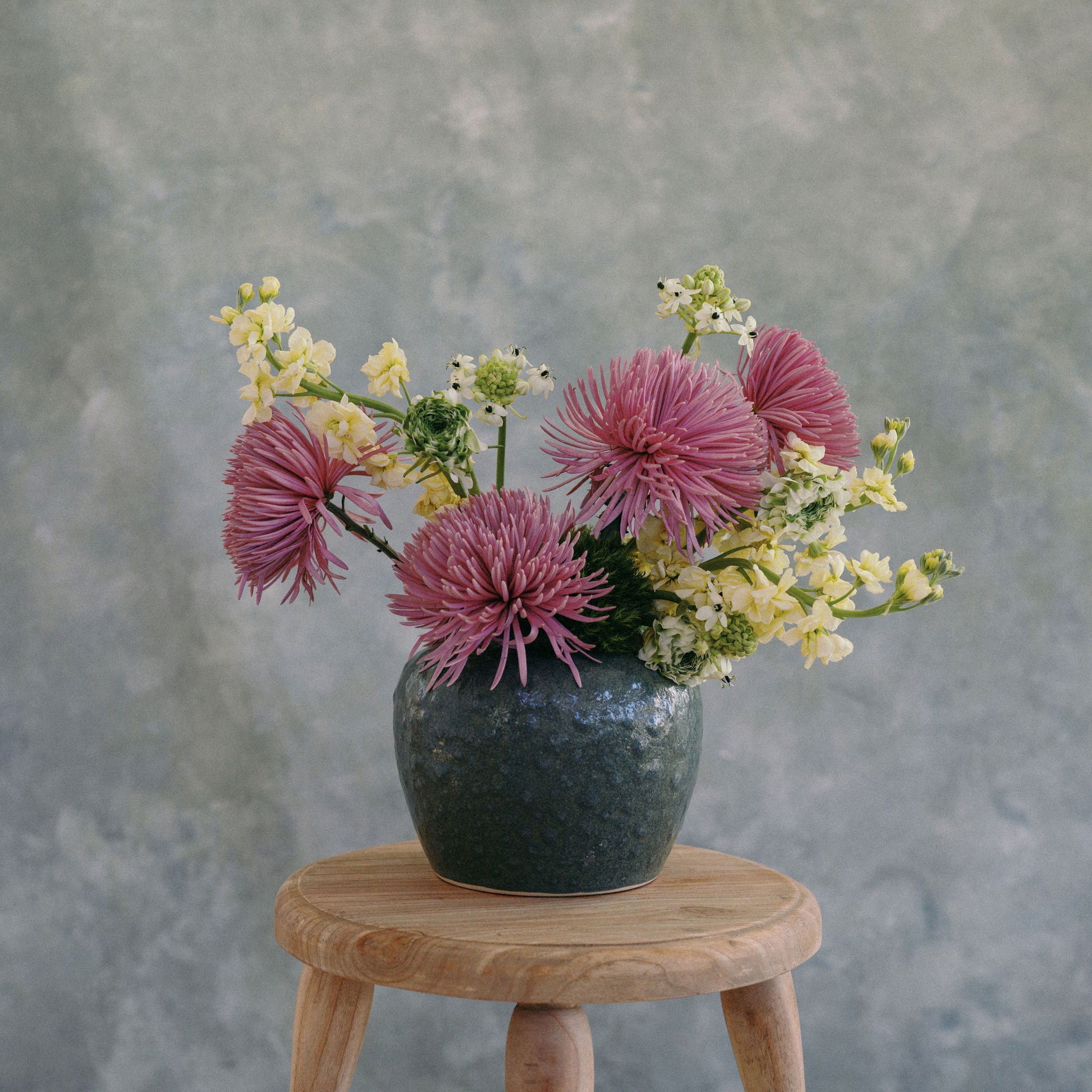 Vase with pink and yellow flowers on a wooden stool against a gray background