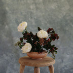 Floral arrangement in a pink vase on a wooden stool against a gray background